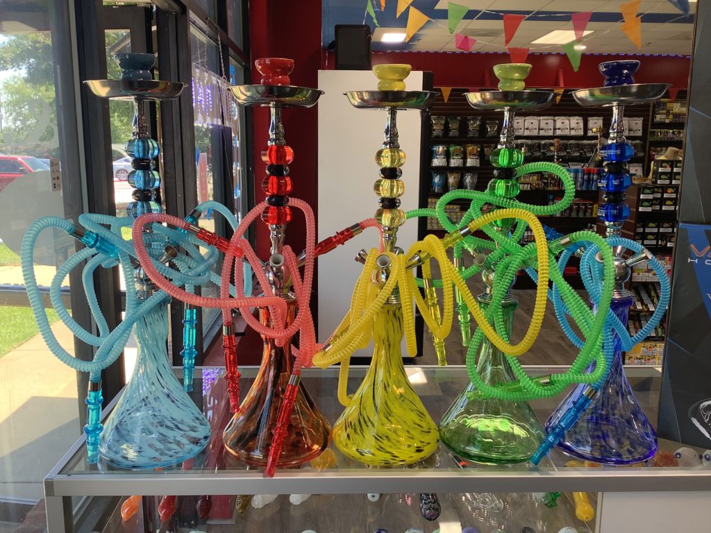 A row of colorful hookahs with matching hoses displayed on a glass shelf inside a store.